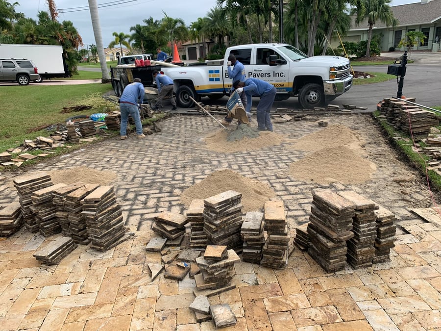 Crew restoring old travertine pavers with fresh mortar in a front courtyard