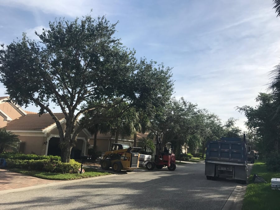 Skid steer and forklift delivering paver pallets to a villa driveway