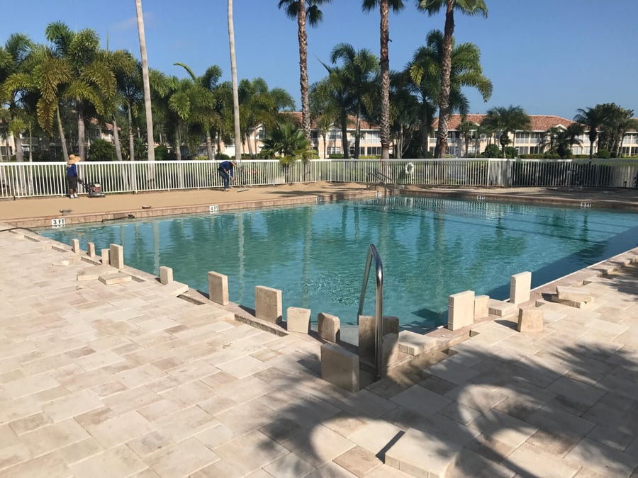 Crew installing travertine pool deck around a community pool