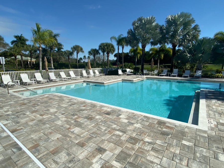 Golf community pool deck in gray tumbled pavers with lounge chairs