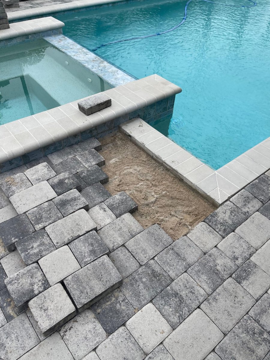 Crew installing gray pavers and coping around a pool and spa