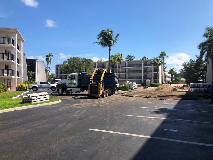 Skid steer and dump truck removing asphalt at a condo parking lot