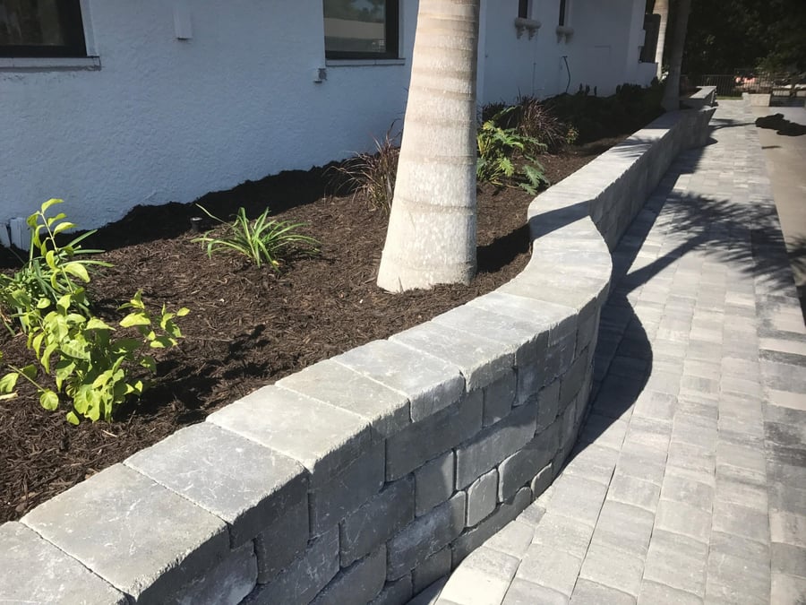 Curved gray paver planter wall beside a paver walkway