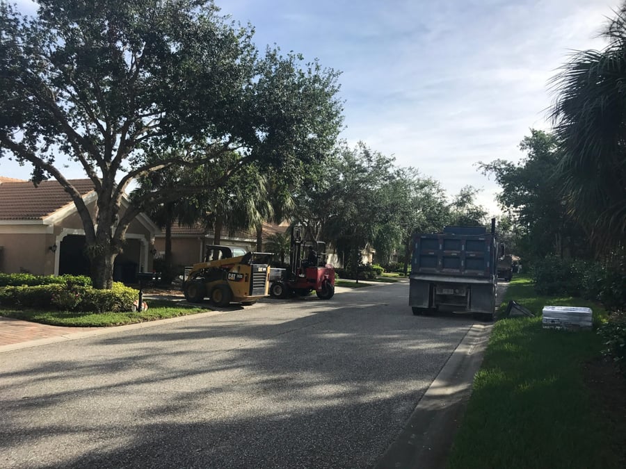Skid steer and dump truck staged on a villa street for a driveway job