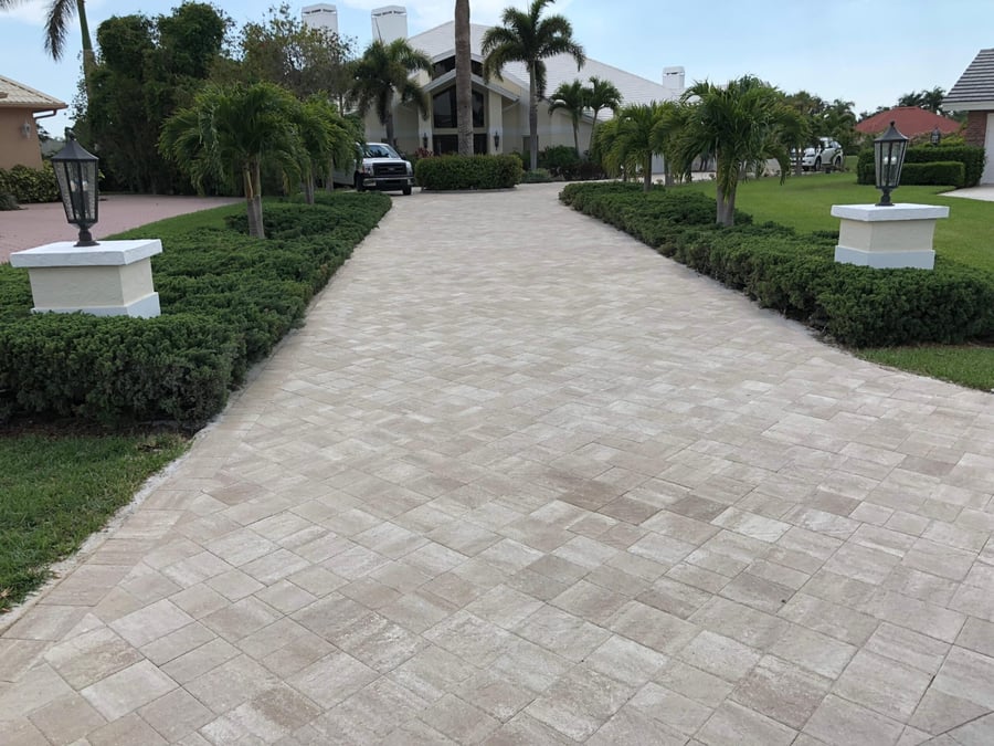 Ivory travertine driveway framed by hedges and lantern piers