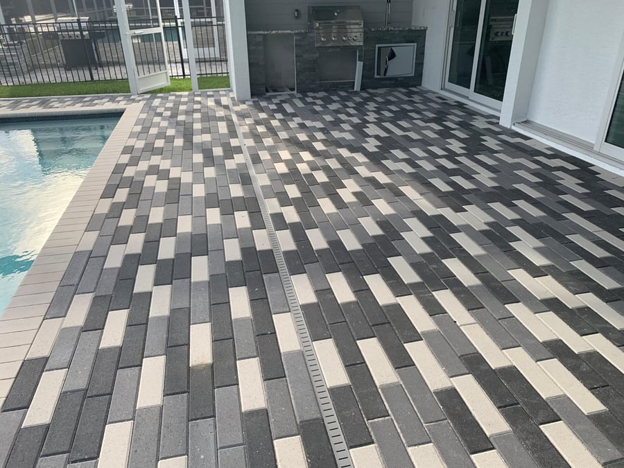 Two-tone brick pool deck beside an outdoor kitchen