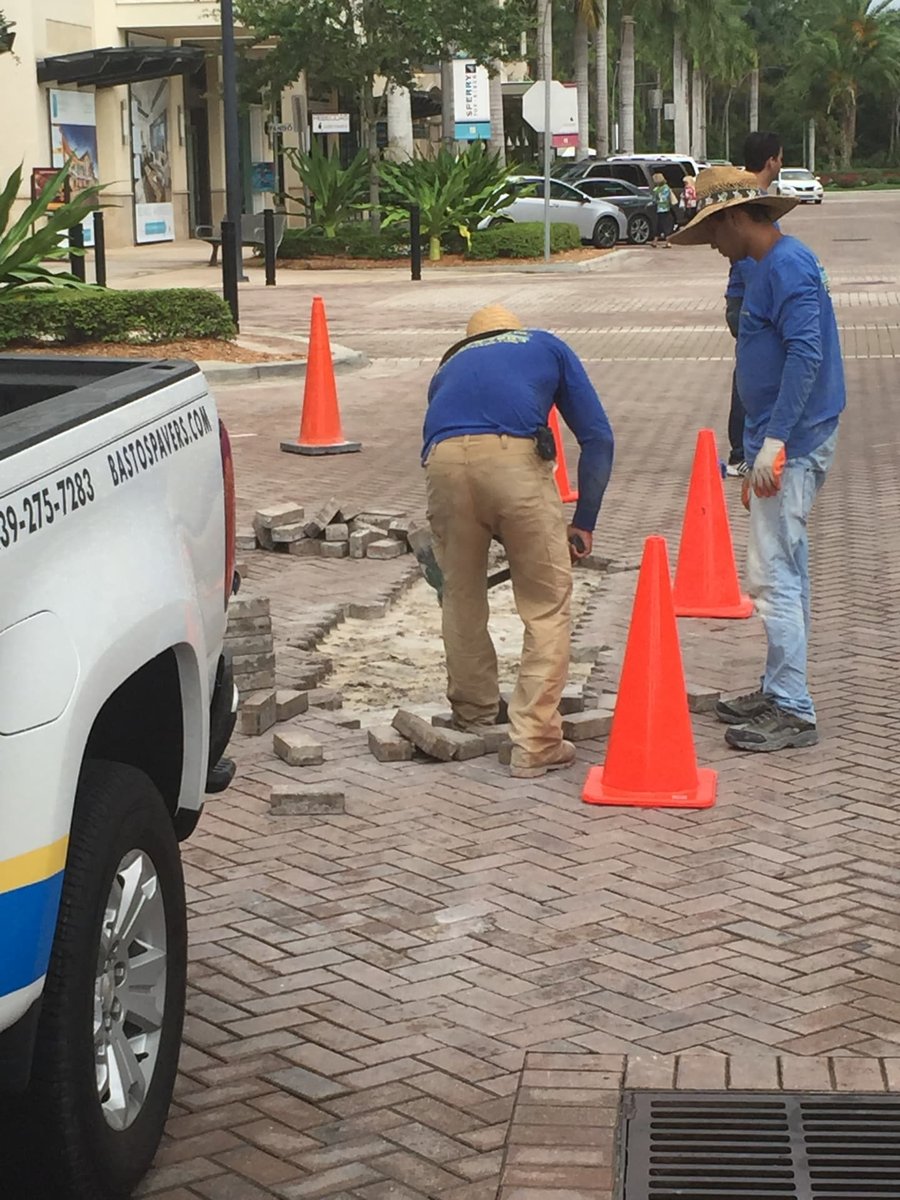 Crew repairing settled pavers on a shopping plaza crosswalk with cones