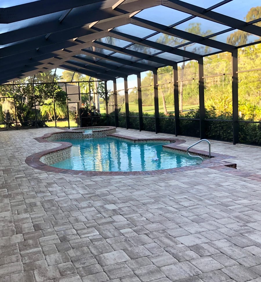 Screened lanai with a large paver pool deck overlooking a golf course