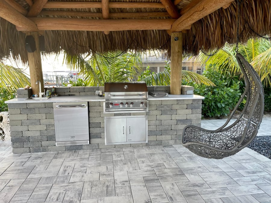 Outdoor kitchen with grill built into a paver wall under a tiki hut