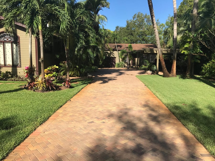 Long herringbone brick driveway framed by tropical landscaping
