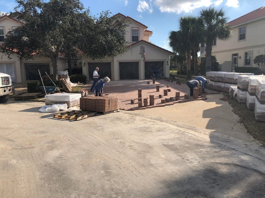 Crew laying brick pavers on a townhome driveway with pallets staged