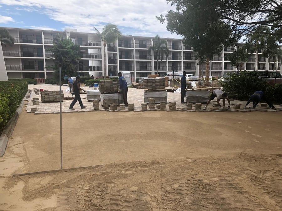 Crew setting pavers across a large condominium courtyard