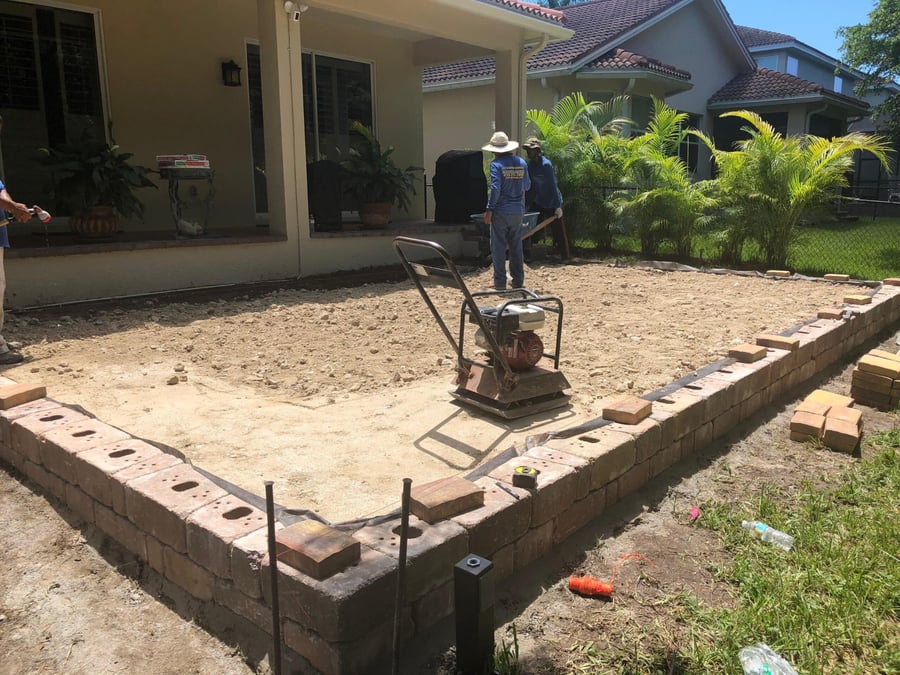 Crew compacting base for a new paver patio behind a home