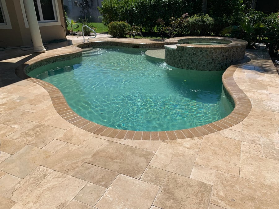 Travertine deck around a freeform pool with raised spa