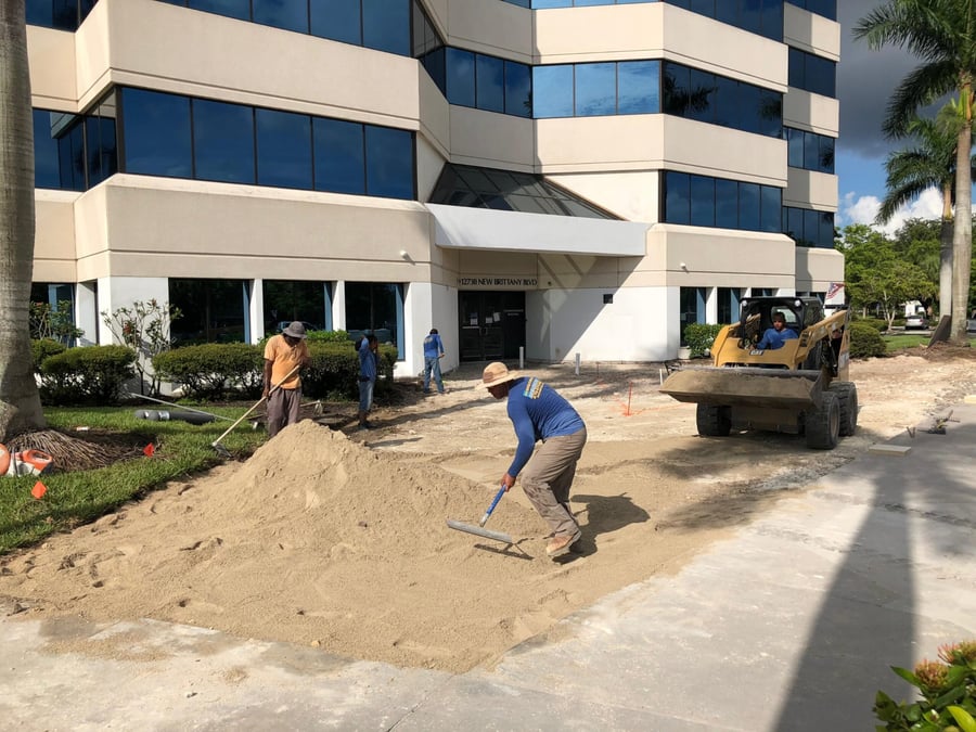 Crew screeding sand at an office tower entrance before paving