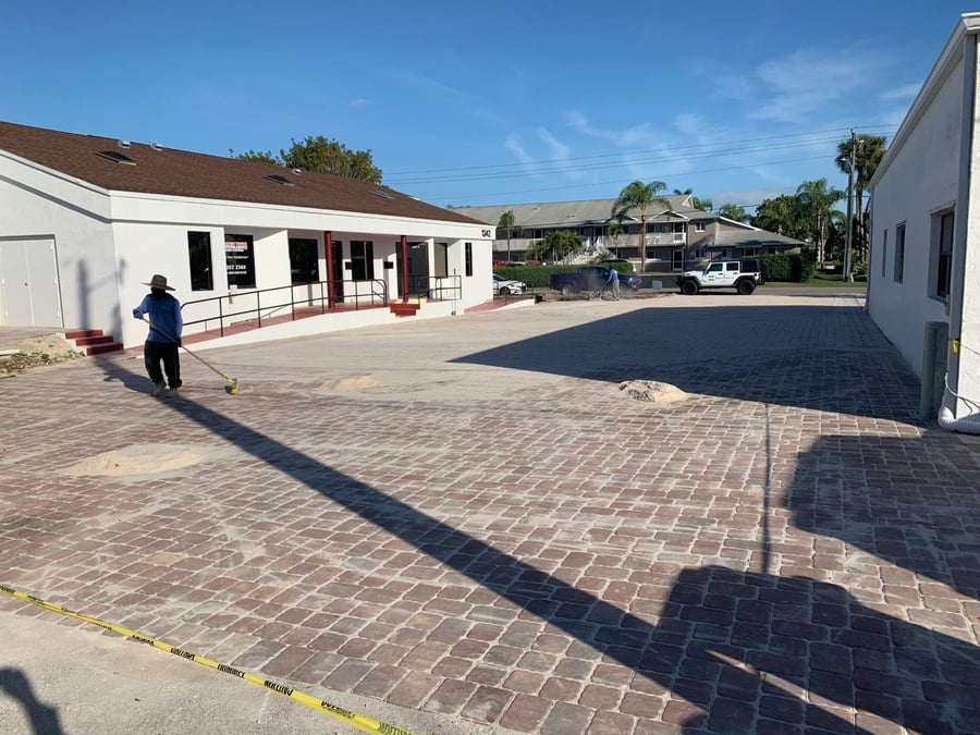 Crew sweeping joint sand across a new cobble paver office parking lot