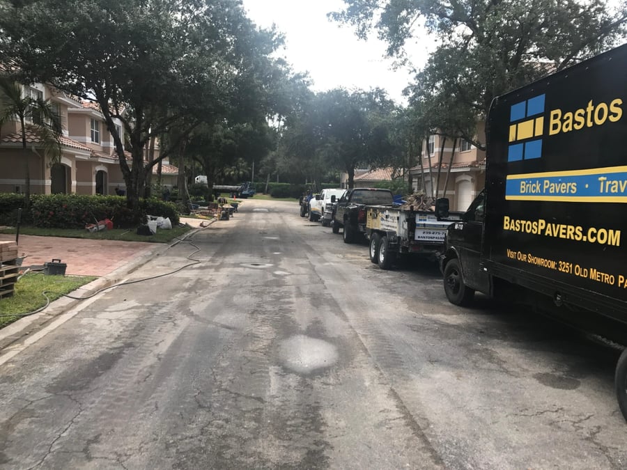 Bastos Pavers trucks and trailers staged on a community street during a driveway project