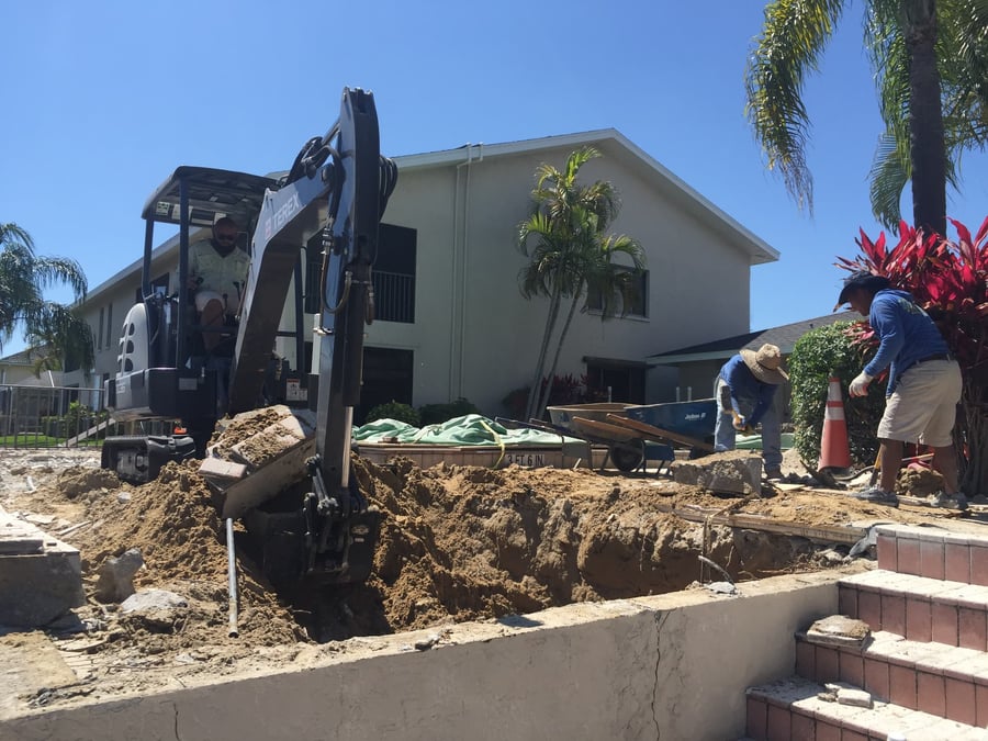 Mini excavator removing settled pavers at a condo pool area