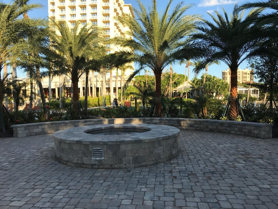 Round paver fire pit with curved seat wall under resort palms