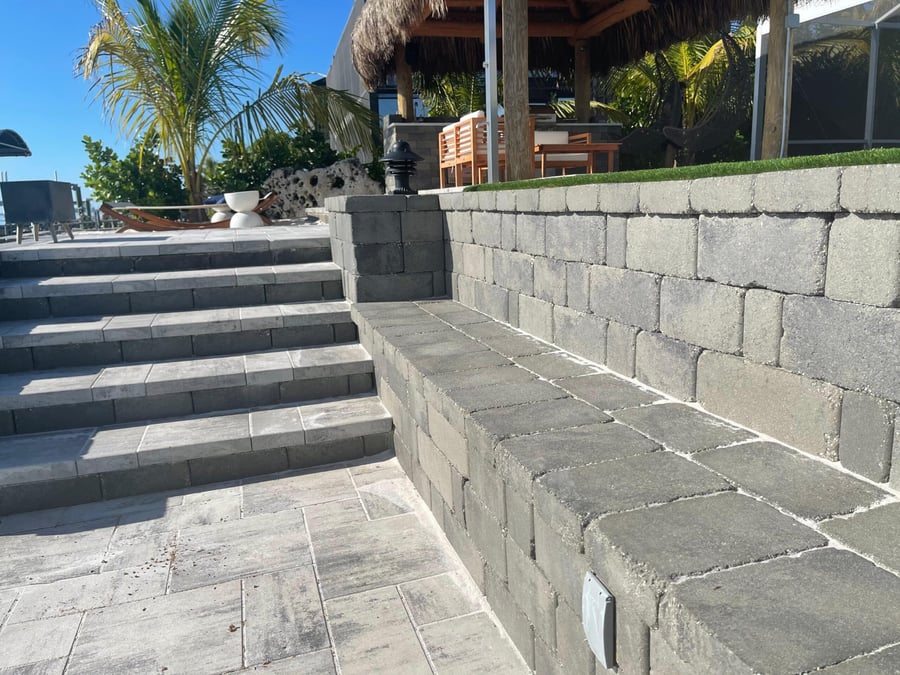 Gray paver retaining wall and steps near a waterfront tiki hut