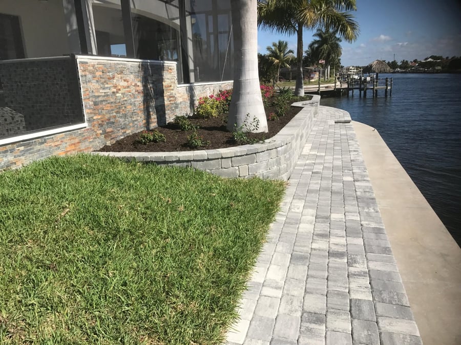 Canal-side paver walkway with a low gray wall and planting bed
