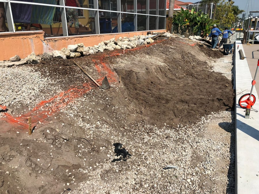 Crew grading base along a seawall before paver installation