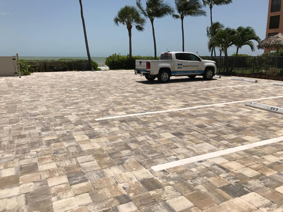 Gulf-front condominium parking lot in travertine-toned pavers with a Bastos truck