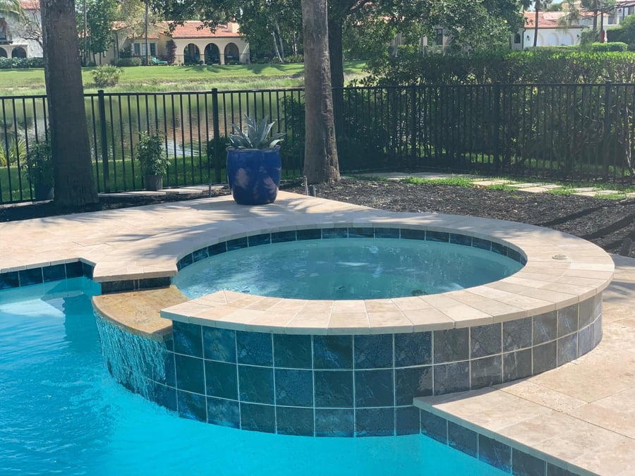 Round spa with travertine coping beside a pool overlooking a lake