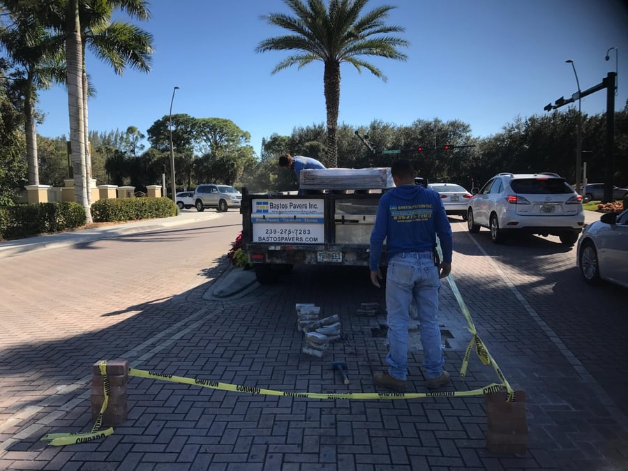 Crew repairing pavers at a gated community entry median