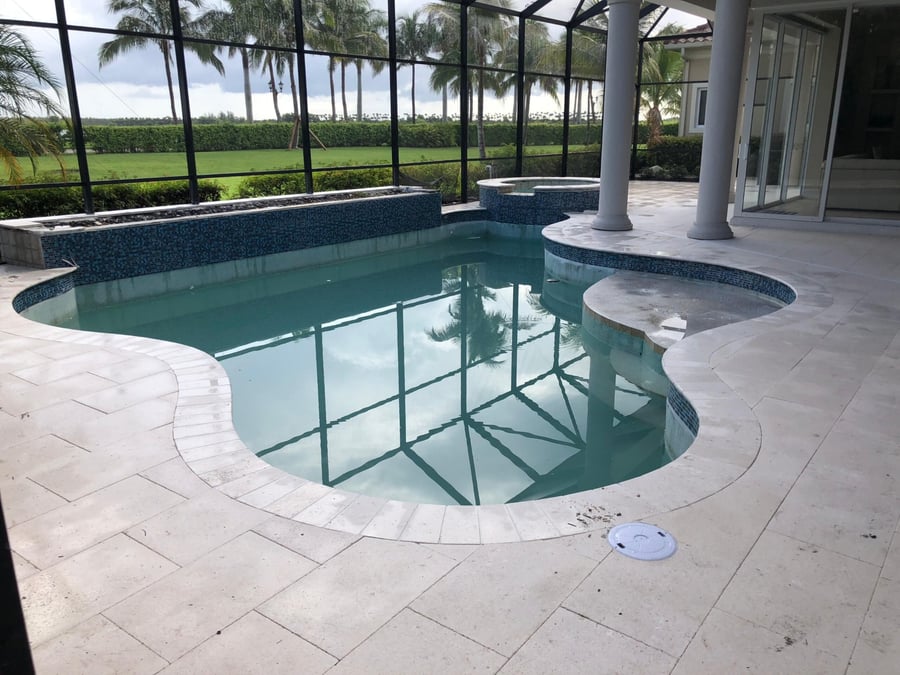 Marble pool deck inside a screened lanai overlooking a golf course