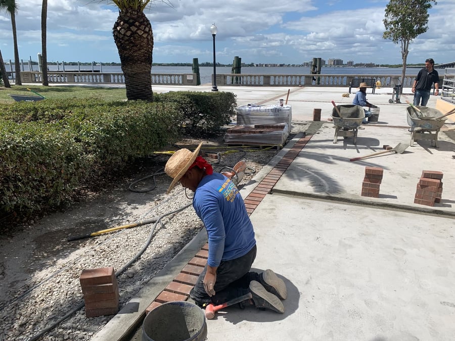 Crew installing red brick banding at a riverfront promenade