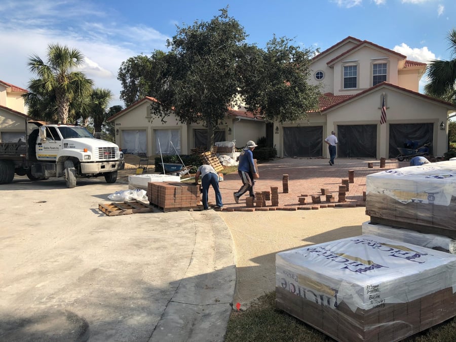 Crew laying red brick pavers on a villa driveway with Bastos truck on site