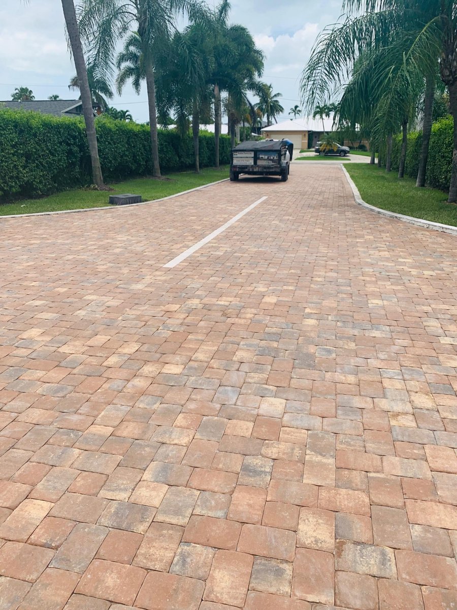 Long terracotta-toned paver driveway lined with royal palms
