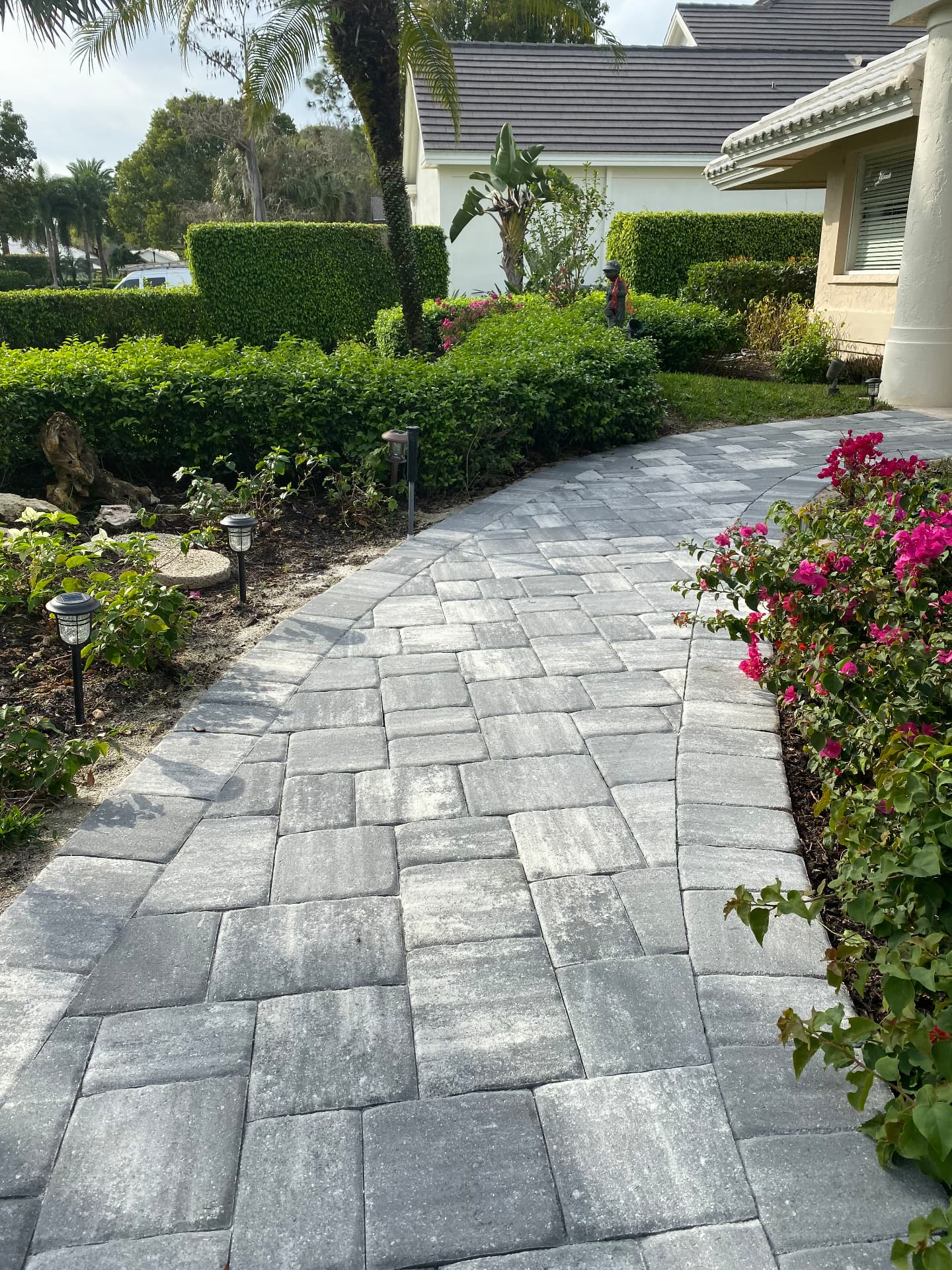 Gray paver walkway winding through hedges to a home entry