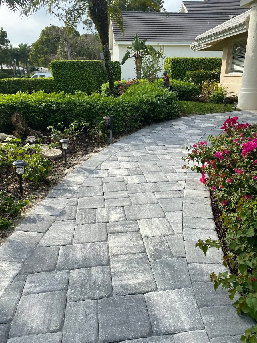 Gray paver walkway winding through hedges to a home entry