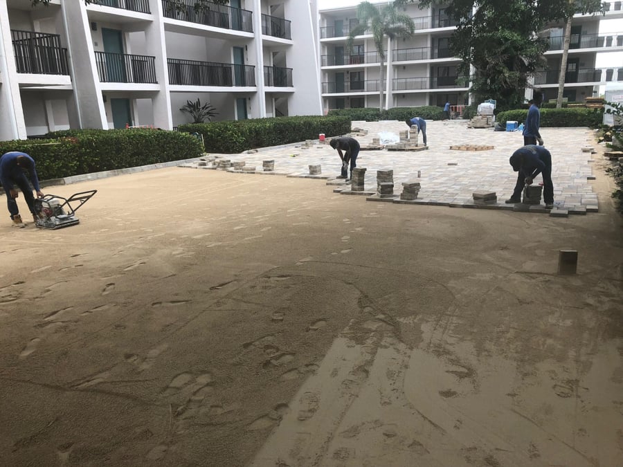 Crew compacting sand and laying pavers in a condominium courtyard
