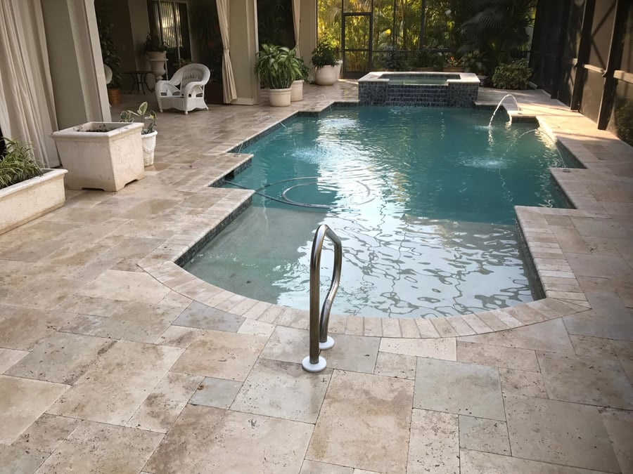 Travertine pool deck inside a screened lanai with spa