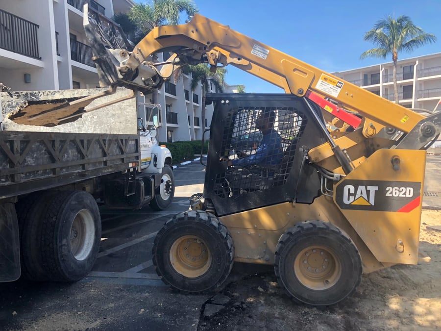 Skid steer loading old asphalt into a Bastos dump truck at a condo lot
