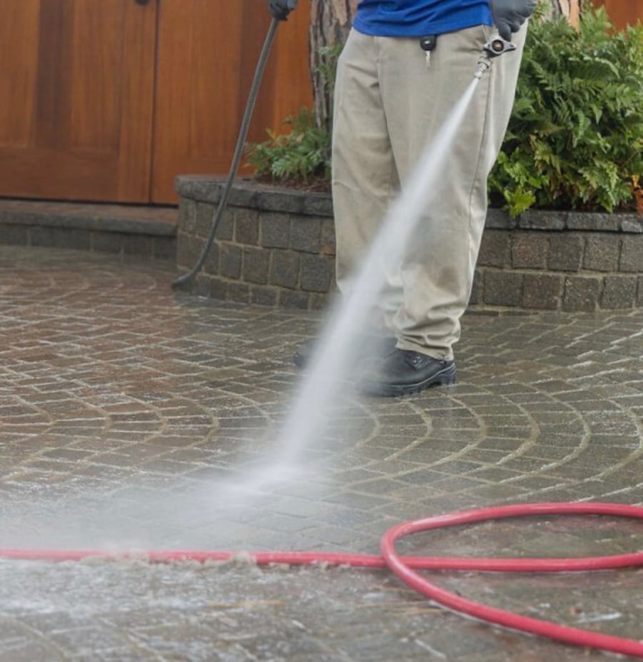 Technician pressure washing cobblestone pavers with a wand
